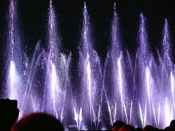Das Bild zeigt Impressionen vom Wasserspiel "Wasserfee". Zu sehen sind lila Fontänen.