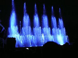 Das Bild zeigt Impressionen vom Wasserspiel "Wasserfee". Zu sehen sind blaue mehrstöckige Fontänen.